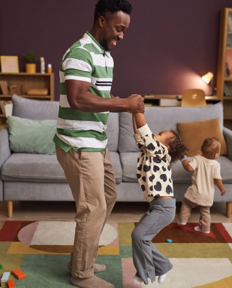 Vertical full length portrait of happy Black father dancing with cute little girl at home in living room